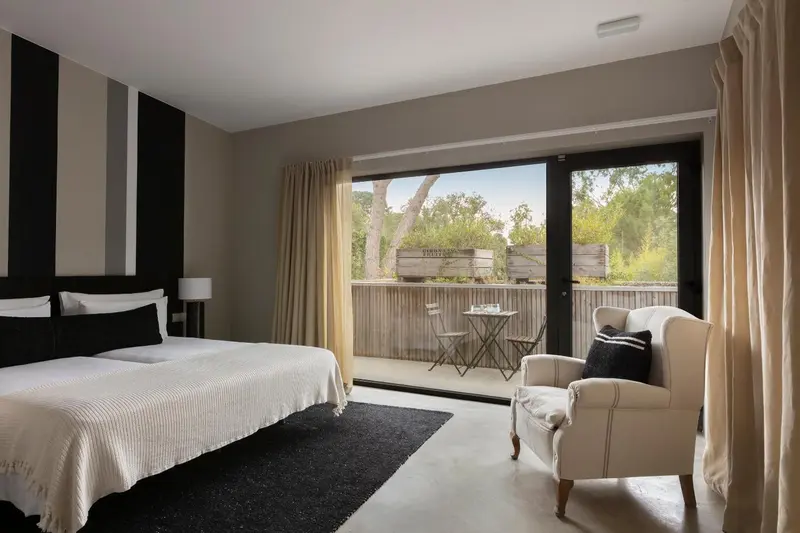 Une chambre lumineuse avec un lit blanc et un fauteuil beige.