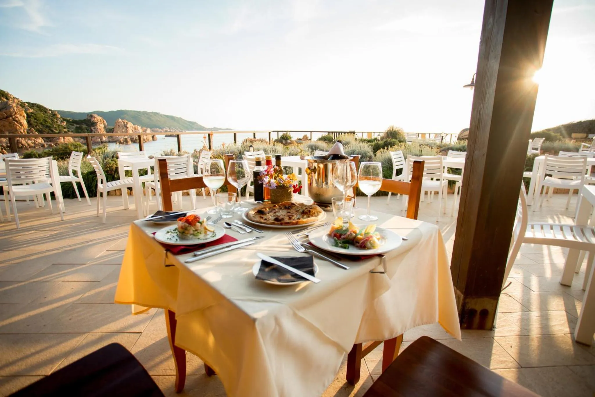 Une table dressée avec des plats et des boissons en terrasse avec vue sur la mer.