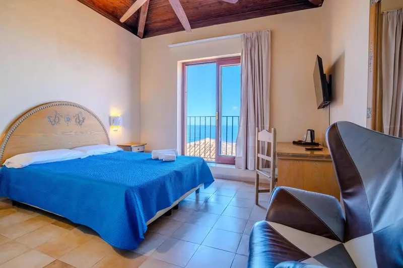 Chambre lumineuse avec un lit recouvert d'une couverture bleue et un accès à un balcon.