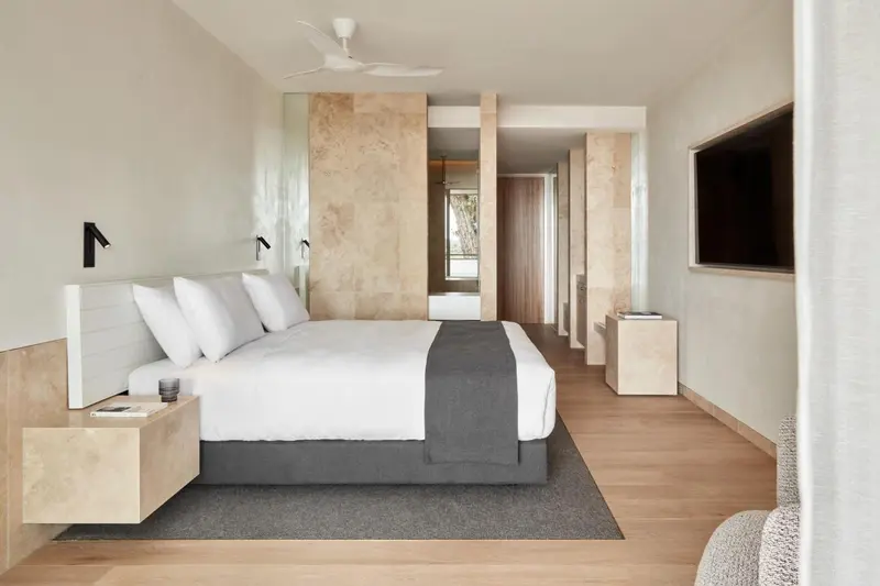 Une chambre lumineuse avec un grand lit recouvert d'une courtepointe grise.