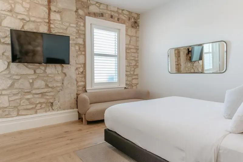 Une chambre lumineuse avec un lit blanc et un mur en pierre.