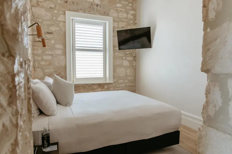 Une chambre lumineuse avec un lit blanc et un mur en pierre.