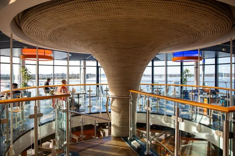 Vue d'un espace circulaire avec une structure en bois au centre et de larges baies vitrées donnant sur la mer.