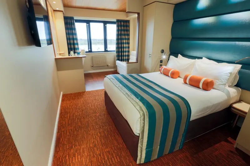 Une chambre lumineuse avec un grand lit et un parquet clair.