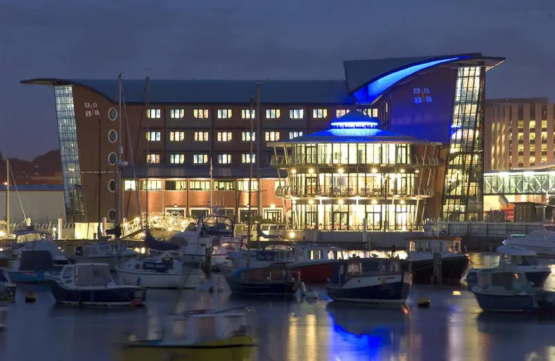 Bâtiment moderne illuminé au bord d'un port de plaisance la nuit.