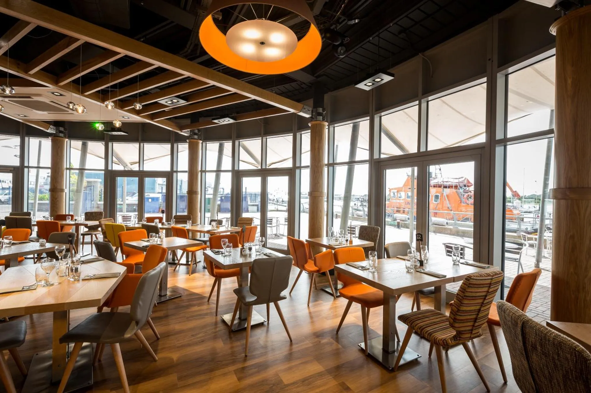 Une salle de restaurant lumineuse avec de grandes baies vitrées donnant sur un port.