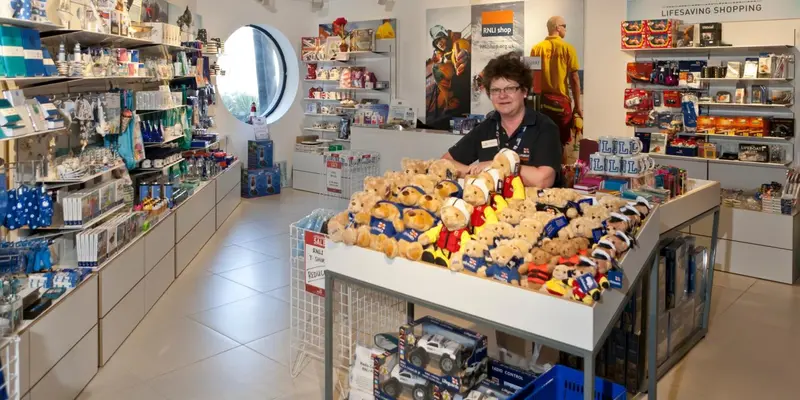 Une employée se tient derrière un comptoir rempli de peluches dans une boutique lumineuse.