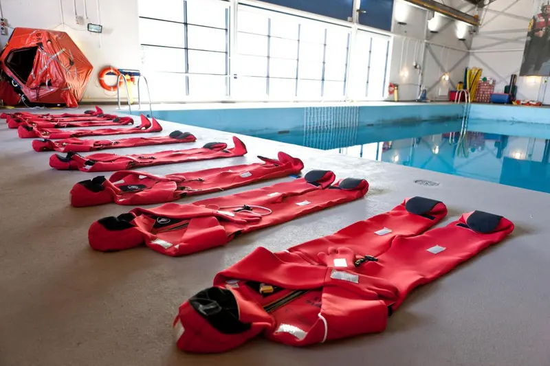 Rangées de gilets de sauvetage rouges reposant sur une surface claire près d'une piscine intérieure.