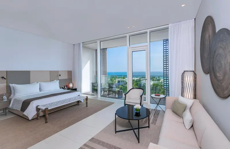 Une chambre lumineuse avec un grand lit et un coin salon donnant sur la mer.