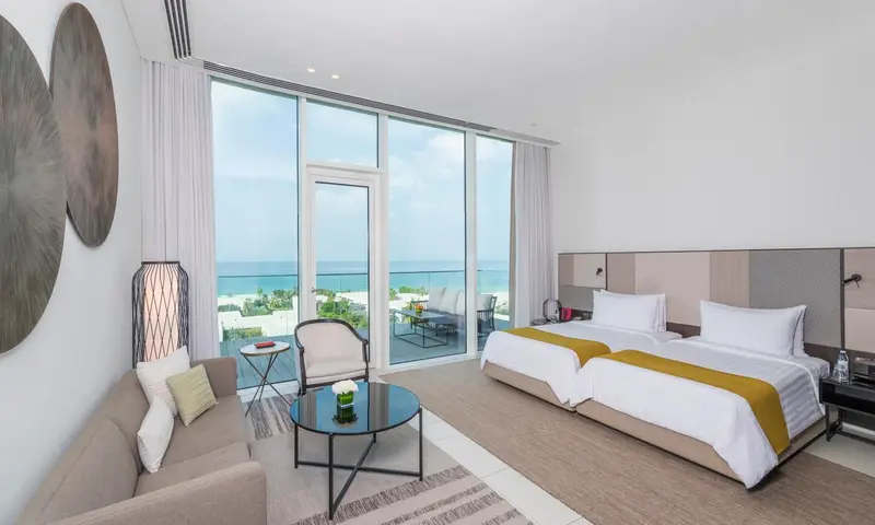 Chambre lumineuse avec canapé, table basse et vue sur la mer depuis un balcon.