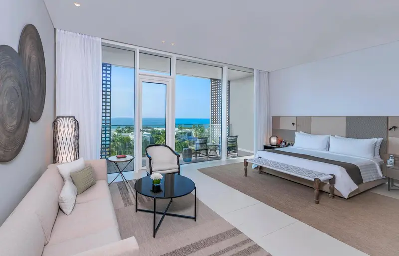 Une chambre lumineuse avec un grand lit et un coin salon donnant sur une vue mer.