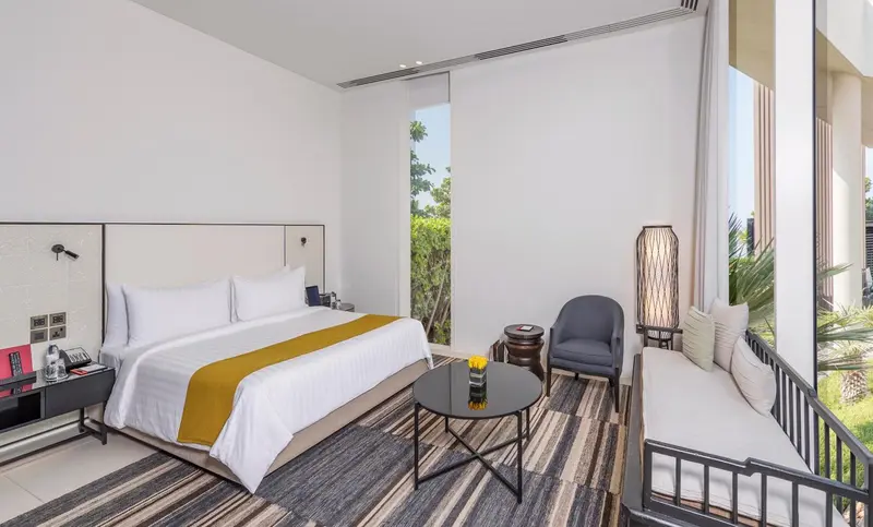 Chambre lumineuse avec un grand lit et un coin salon près d'une fenêtre.