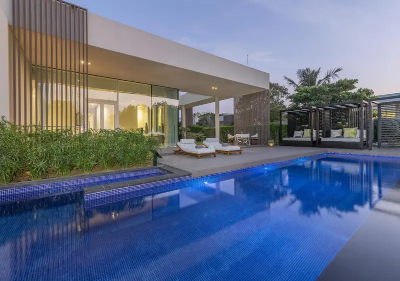 Une piscine bleue reflète un bâtiment moderne avec de grandes baies vitrées et une terrasse aménagée.