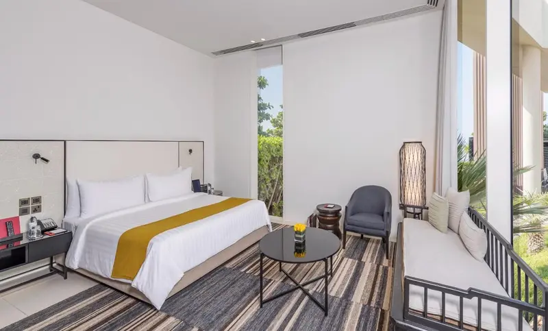Une chambre lumineuse avec un grand lit et un coin salon près d'une fenêtre.
