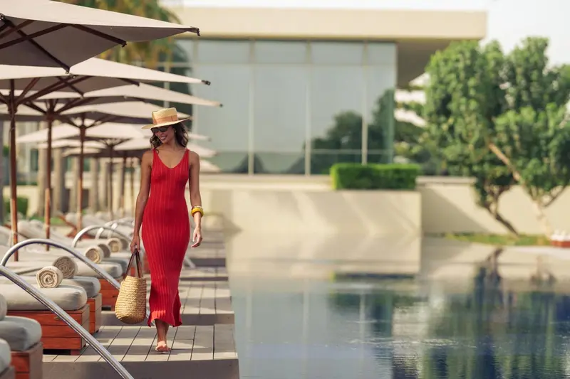 Une femme se promène le long d'une piscine bordée de transats.