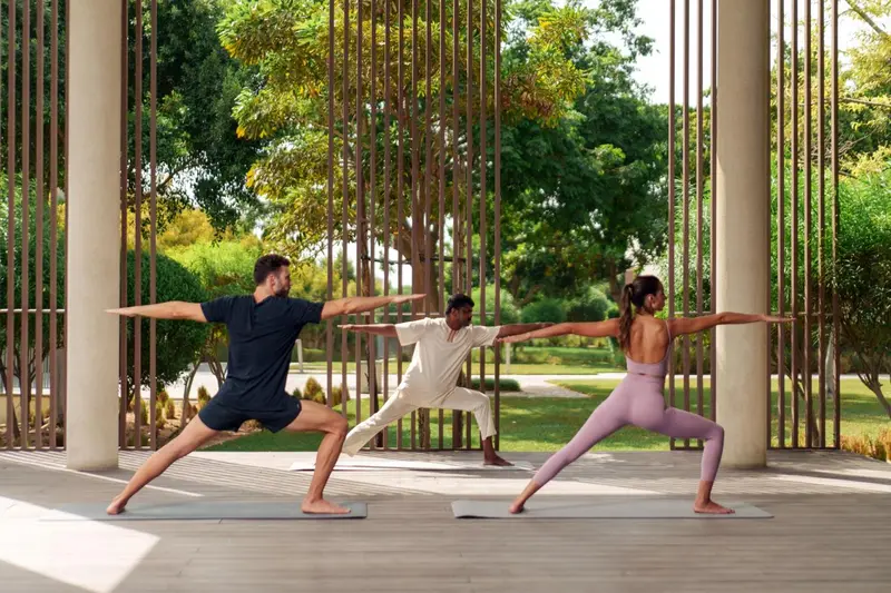Trois personnes pratiquent le yoga sur des tapis dans un espace extérieur couvert.