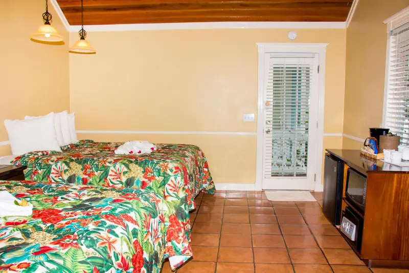 Une chambre lumineuse avec un lit recouvert d'une couette aux motifs tropicaux et une porte-fenêtre.