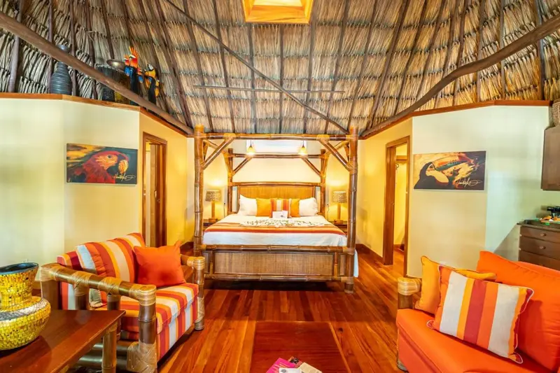 Une chambre lumineuse avec un lit à baldaquin en bois et des fauteuils colorés.