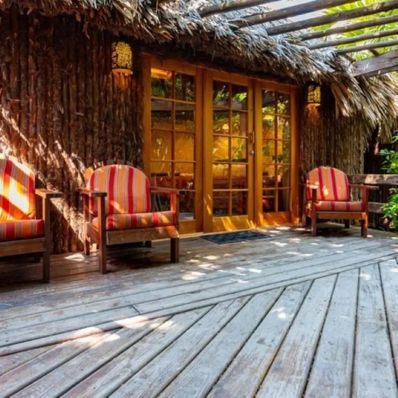 Terrasse en bois avec deux fauteuils à rayures devant une porte vitrée.