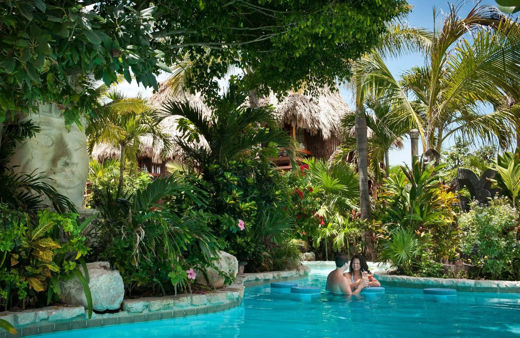 Deux personnes se détendent dans une piscine turquoise entourée d'une végétation luxuriante.