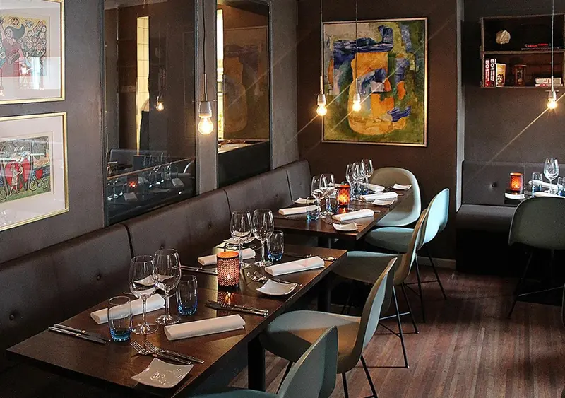 Une salle de restaurant avec des tables dressées et des suspensions lumineuses.