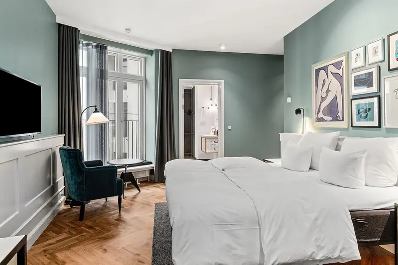 Une chambre lumineuse avec un grand lit et un fauteuil vert.