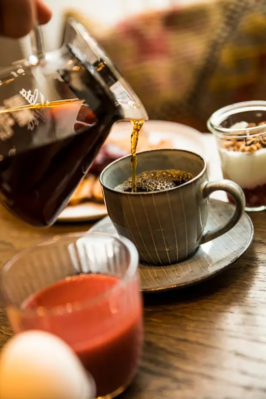 Une tasse de café est remplie par une verseuse en verre sur une table en bois.