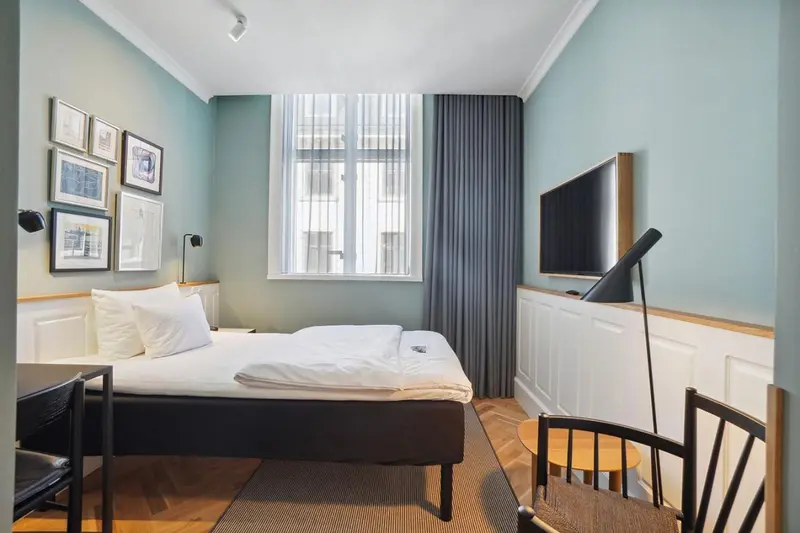 Une chambre lumineuse avec un lit simple et un téléviseur mural.