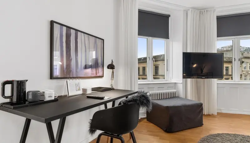 Une pièce lumineuse avec un bureau, une télévision et un coin détente près d'une fenêtre.