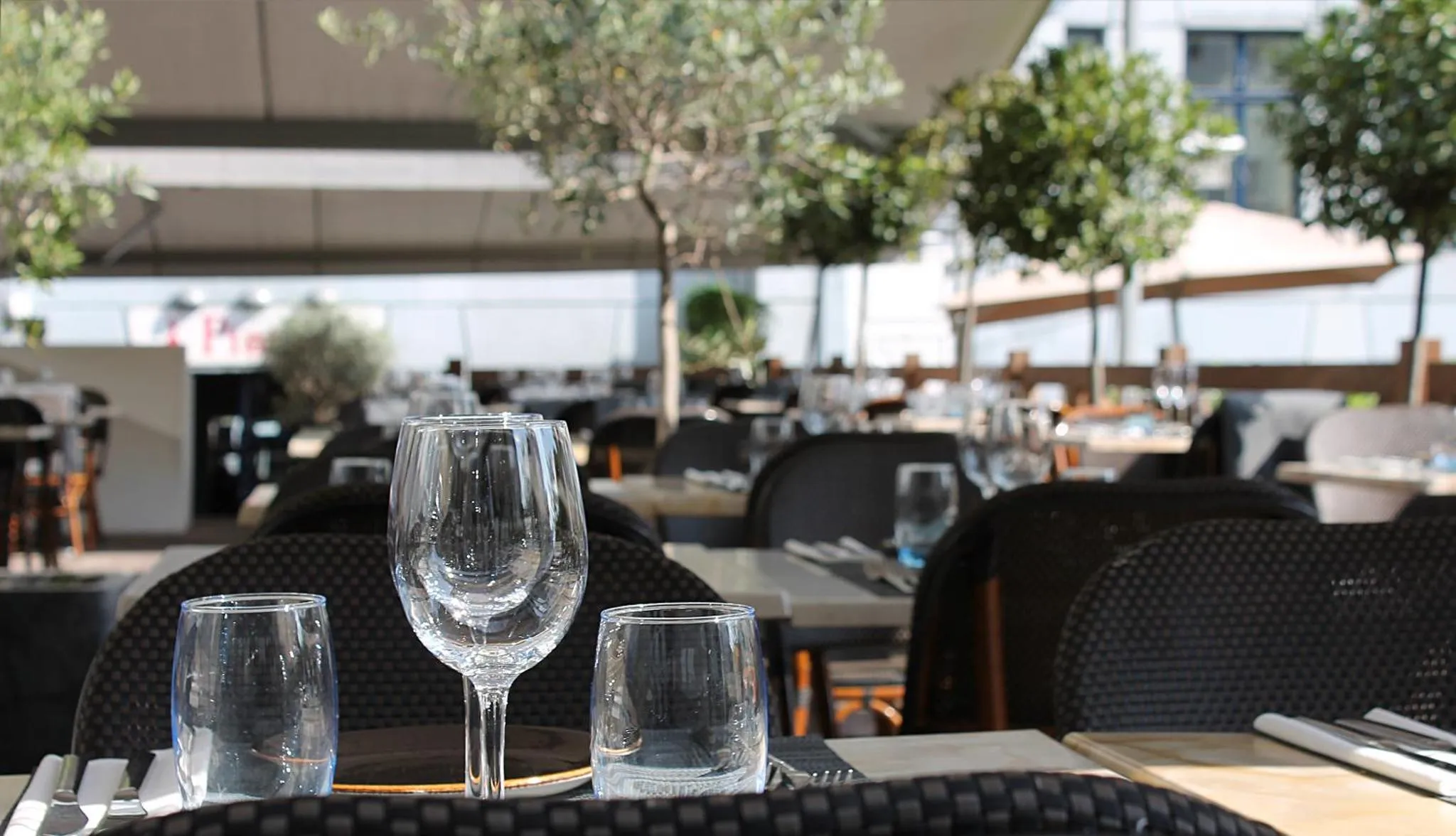 Une table est dressée avec des verres et de la vaisselle sur une terrasse ensoleillée.
