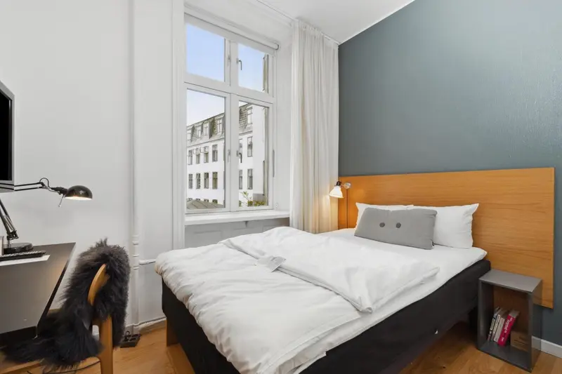 Une chambre lumineuse avec un lit simple et une vue sur la ville.