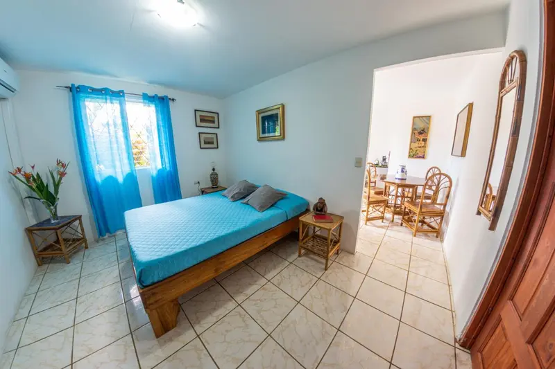 Une chambre lumineuse avec un lit turquoise et un coin repas en rotin.