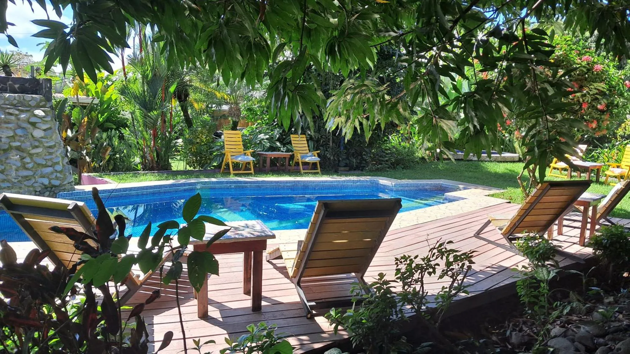 Transats en bois disposés autour d'une piscine rectangulaire dans un jardin tropical.