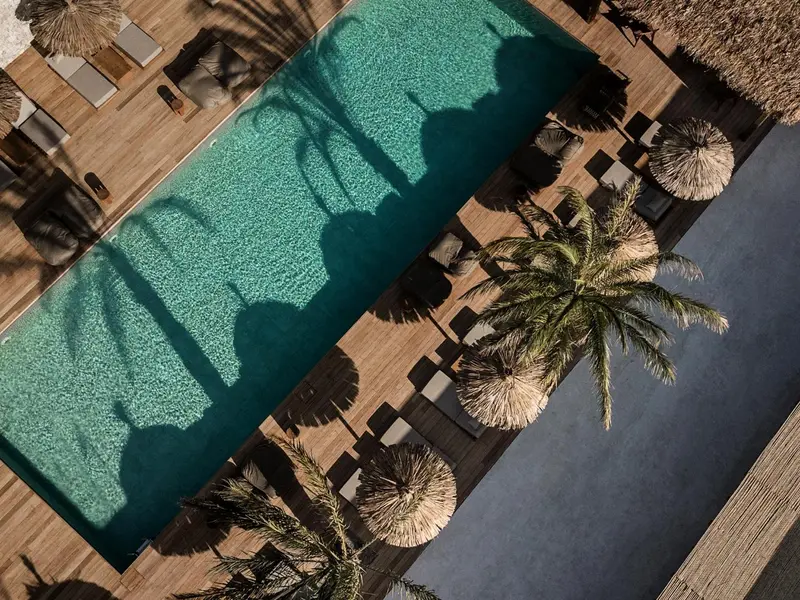 Vue aérienne d'une piscine rectangulaire bordée de chaises longues et de parasols en chaume.