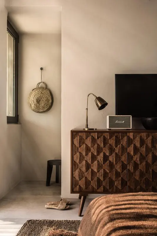 Une chambre sobre avec une commode en bois sculpté et une décoration murale en fibres naturelles.