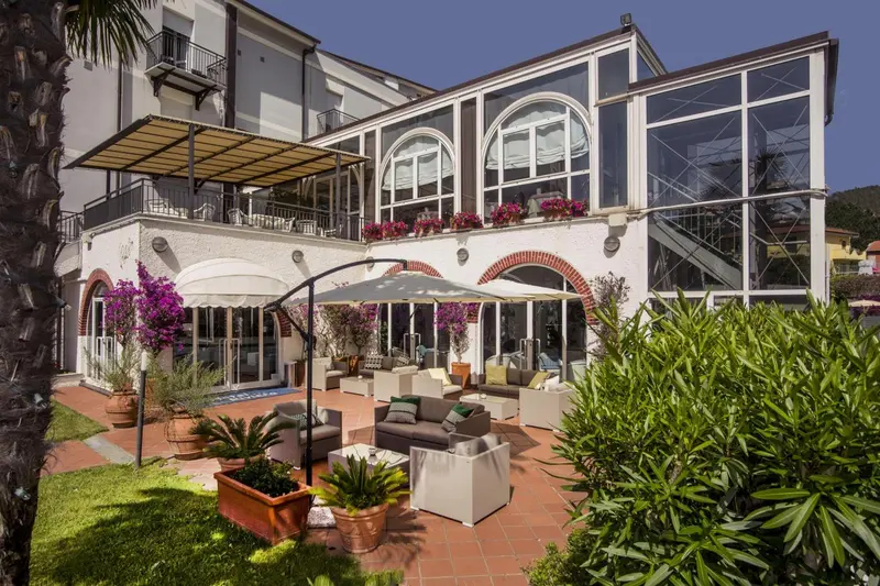 Terrasse ombragée avec mobilier de jardin et végétation luxuriante devant un bâtiment blanc.