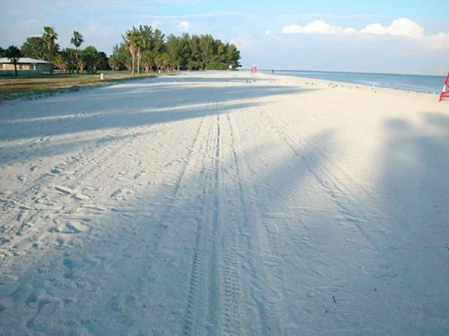 Plage de sable blanc bordée par une mer bleue sous un ciel nuageux.
