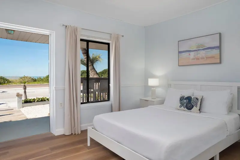 Chambre lumineuse avec un lit blanc et une vue sur la mer.