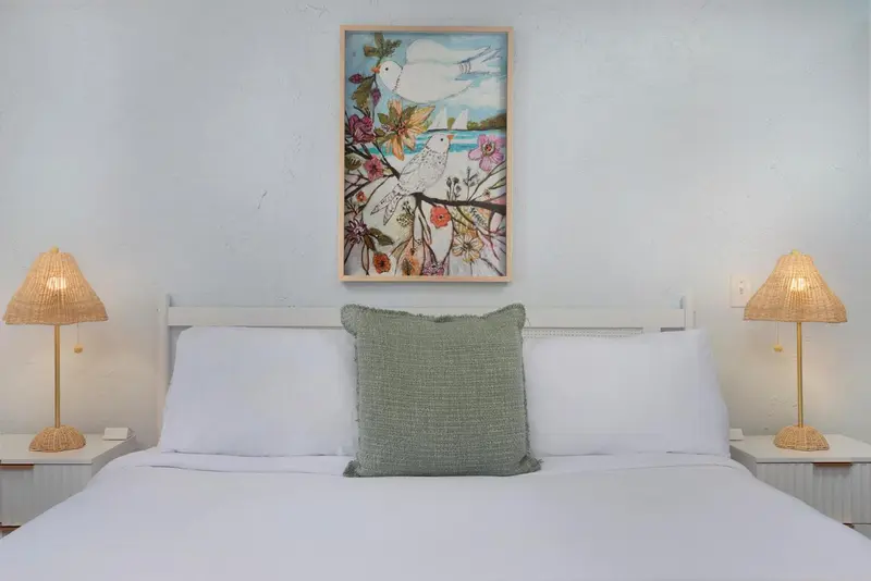 Un lit blanc avec des oreillers et un tableau floral au-dessus.