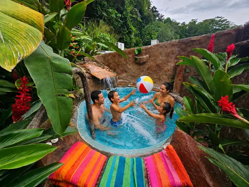 Une famille s'amuse dans un bassin d'eau entouré de végétation tropicale.