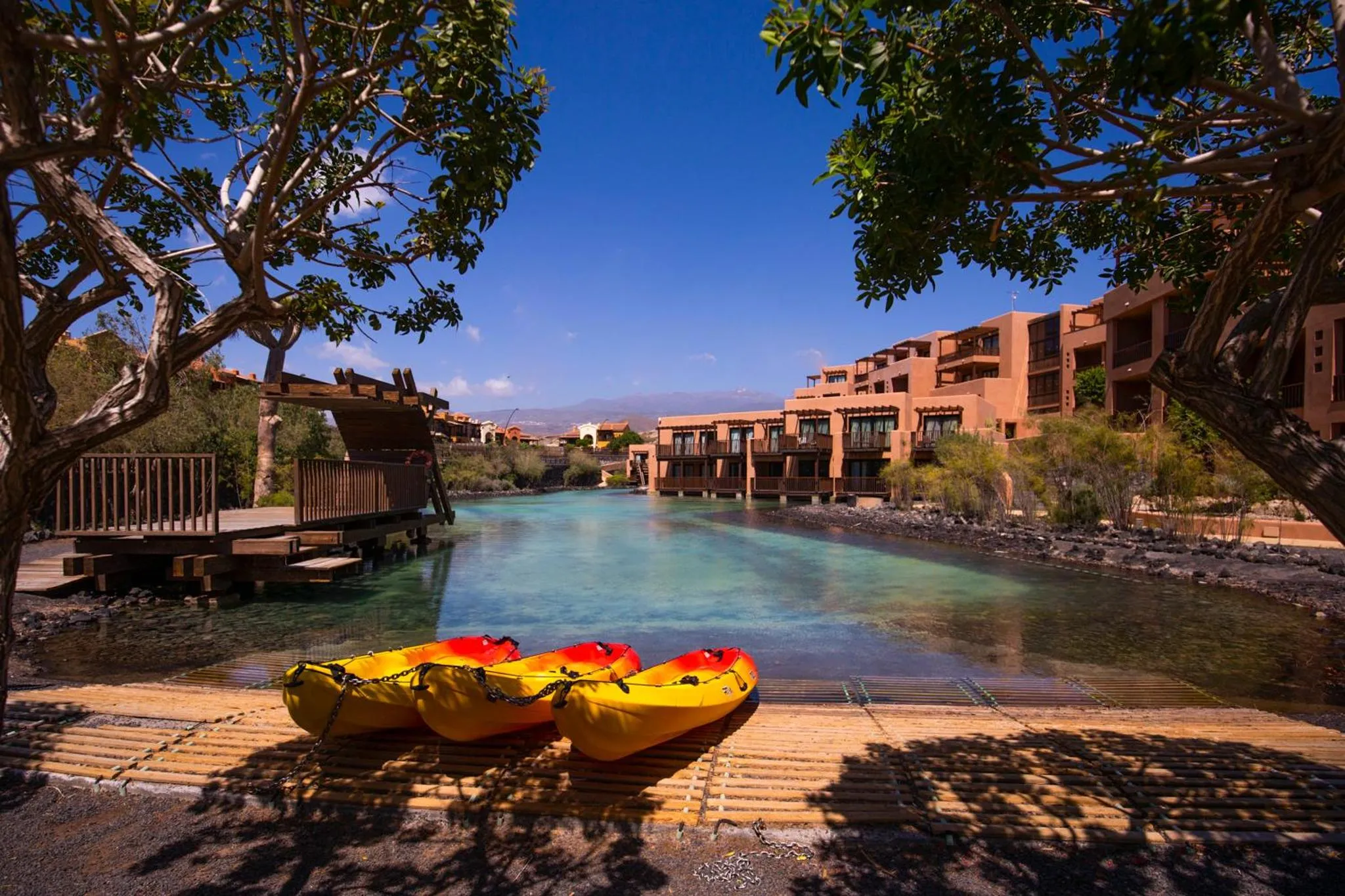Trois kayaks jaunes reposent sur une plage de sable sombre au bord d'un canal d'eau turquoise.
