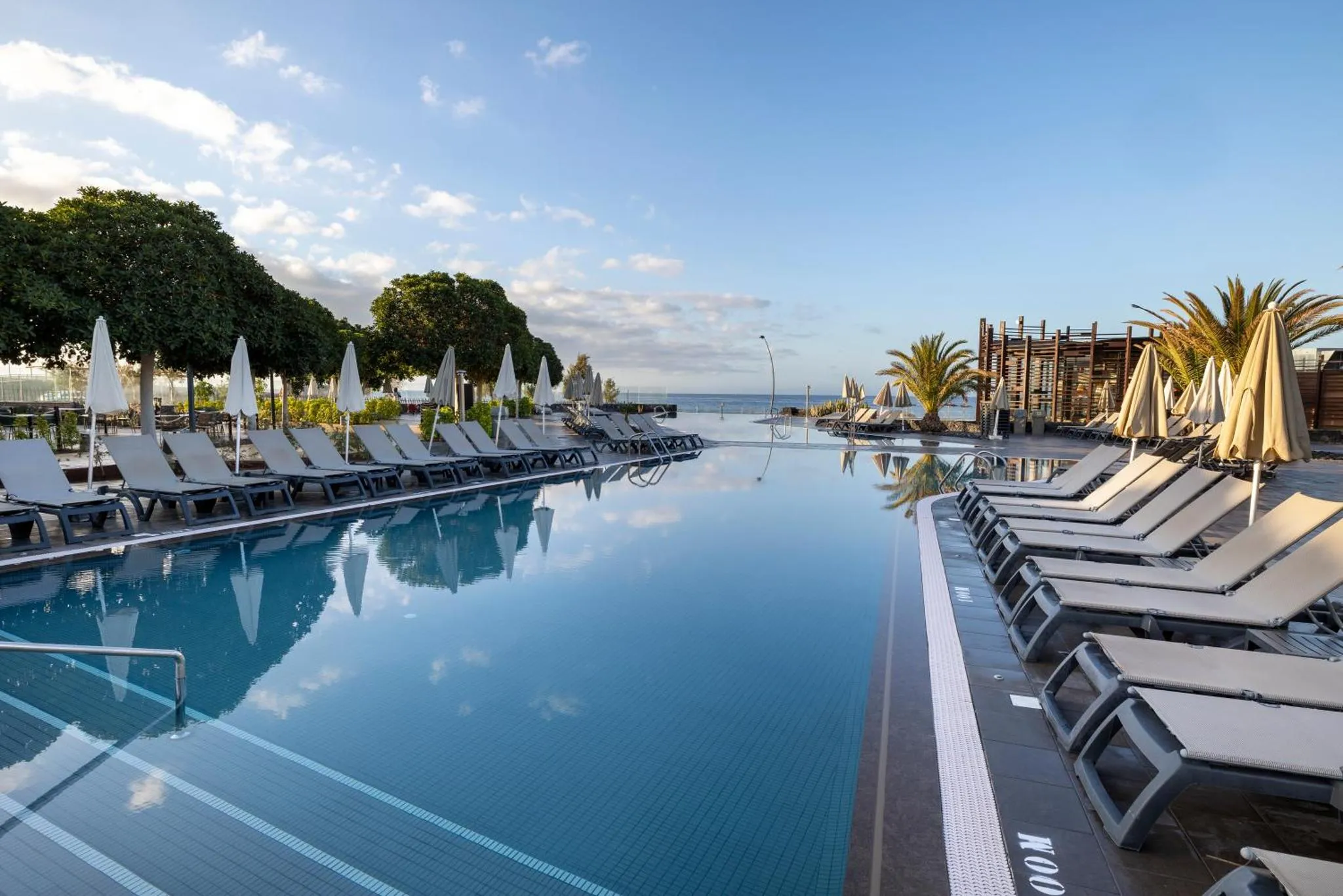 Transats blancs alignés au bord d'une piscine à débordement avec vue sur la mer.