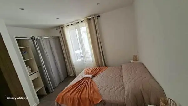 Une chambre avec un lit recouvert d'une couverture orange et des rideaux clairs.