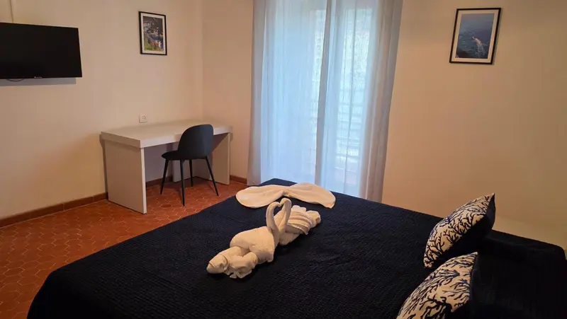Une chambre avec un lit recouvert d'une couverture sombre et un bureau près d'une fenêtre.