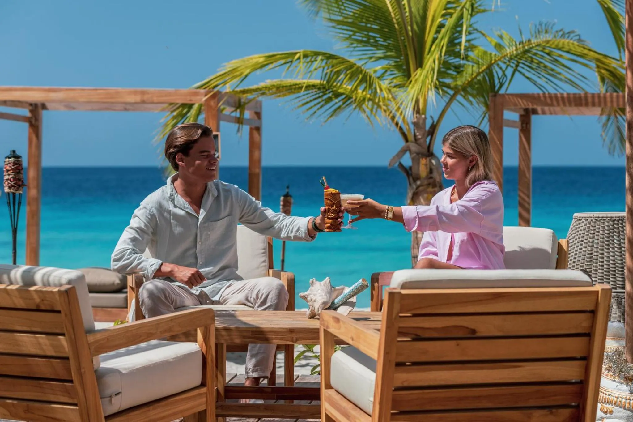 Deux personnes trinquant avec des boissons sur une terrasse en bord de mer.
