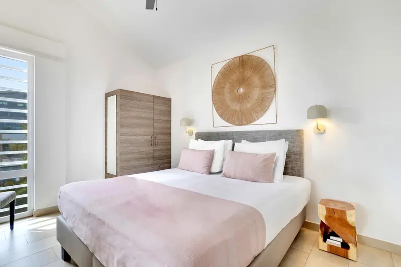 Une chambre lumineuse avec un grand lit recouvert d'une courtepointe rose et d'oreillers.