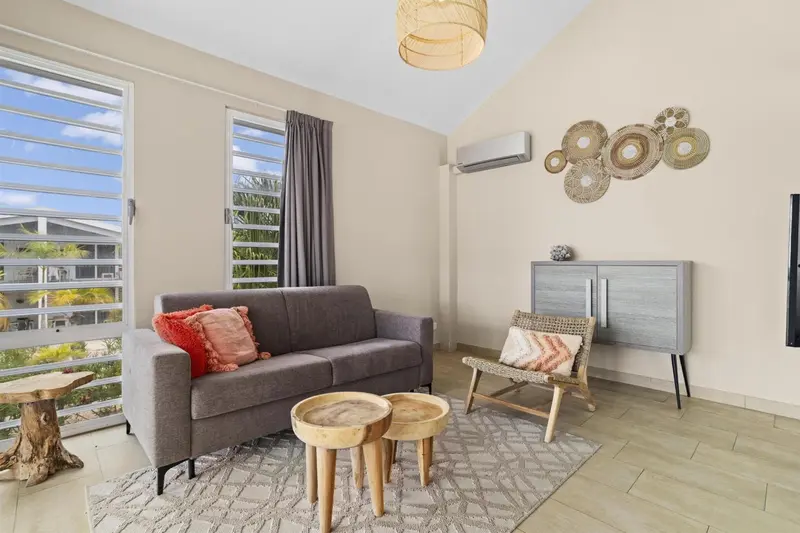 Un salon lumineux avec un canapé gris et une chaise en rotin.