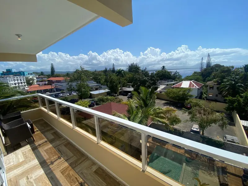 Vue panoramique sur une végétation luxuriante et la mer depuis une terrasse.