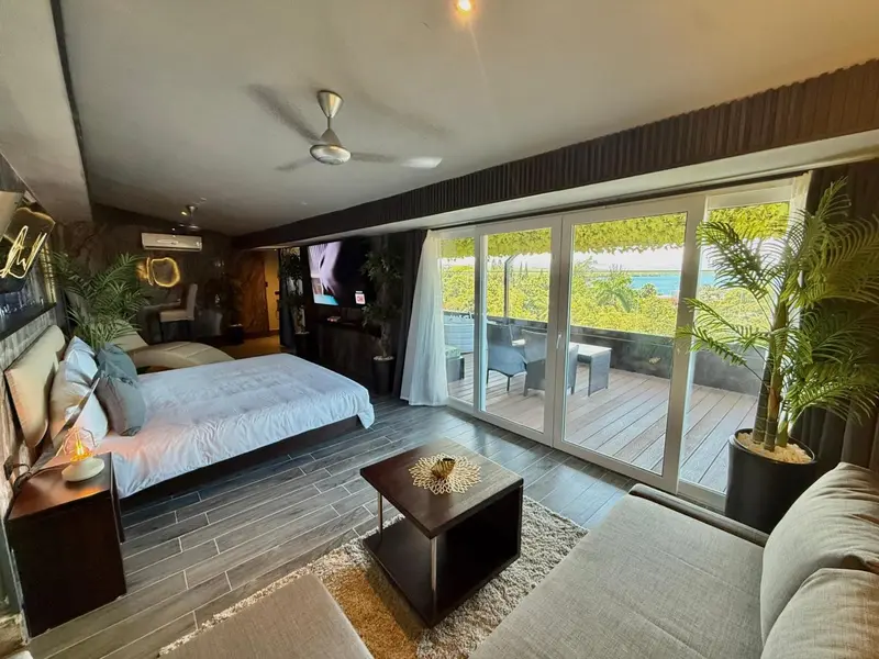 Une chambre spacieuse s'ouvre sur une terrasse avec vue sur la végétation et la mer.