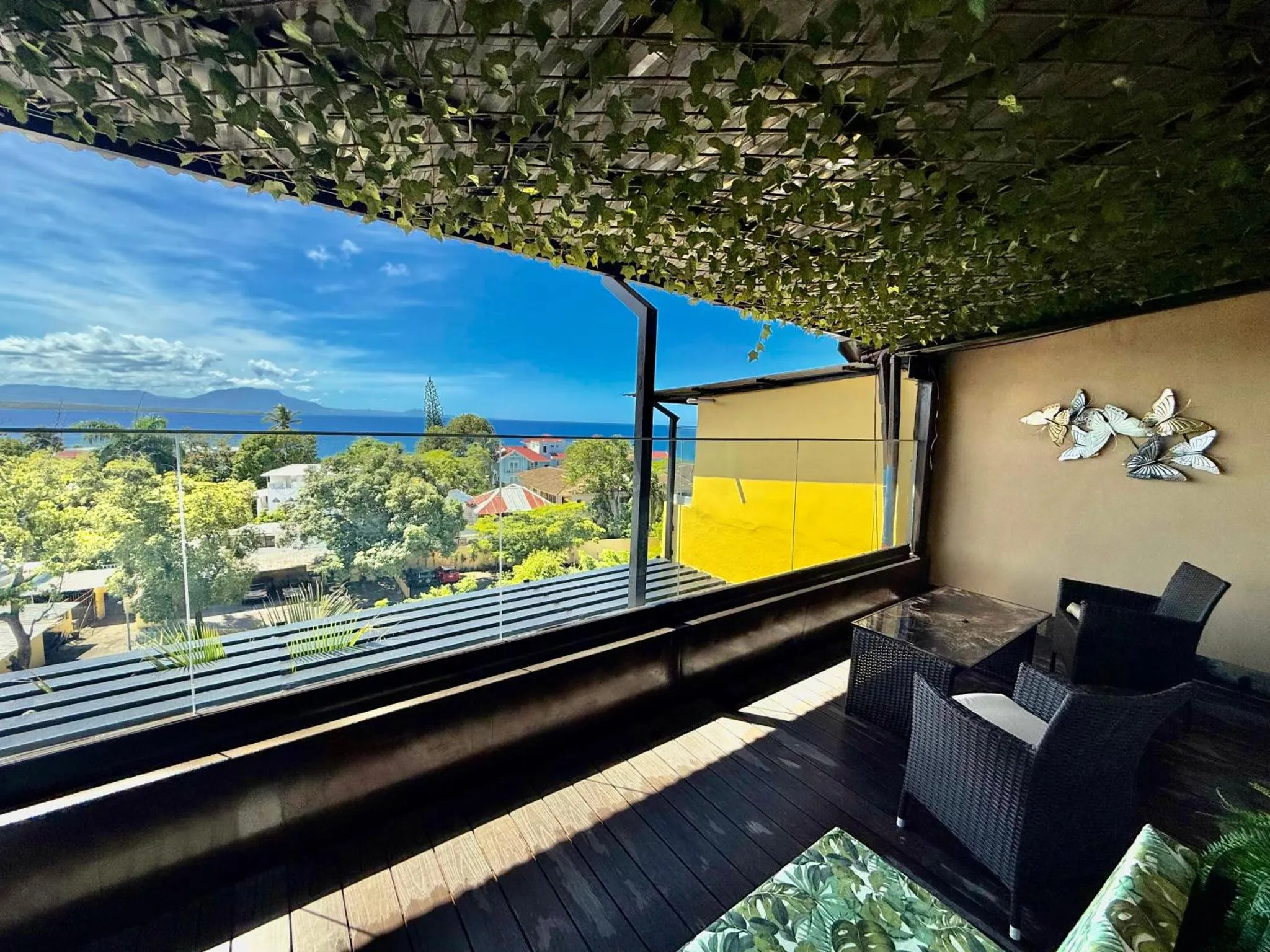 Terrasse ombragée avec mobilier d'extérieur et vue sur la mer et les montagnes.